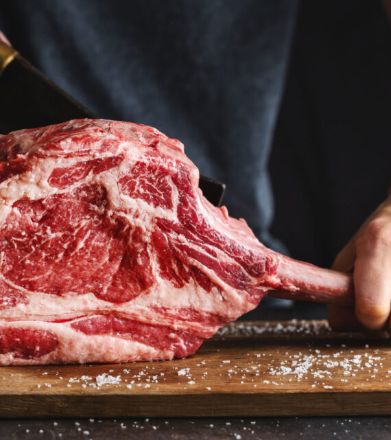 Butcher cuting fresh appetizing tomahawk steak on old wooden board. Closeup